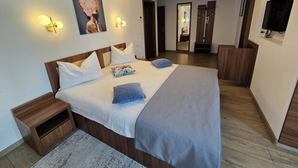 A modern hotel room with a large bed, wooden headboard, and a flat-screen TV mounted on the wall. - Pensiunea Transilvania (Sibiu)