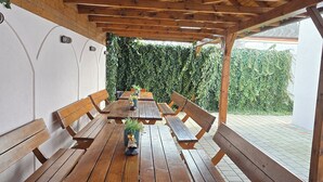A covered outdoor dining area with wooden benches and a central table, surrounded by a hedge wall. - Pensiunea Transilvania (Sibiu)