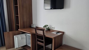 A compact living space with a wooden desk, chair, and bench, a small refrigerator, a TV mounted on the wall, and a patterned rug on the floor. - Pensiunea Transilvania (Sibiu)