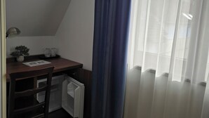 A small, neatly arranged room with a wooden desk, a chair, a radiator, and a window with sheer curtains. - Pensiunea Transilvania (Sibiu)