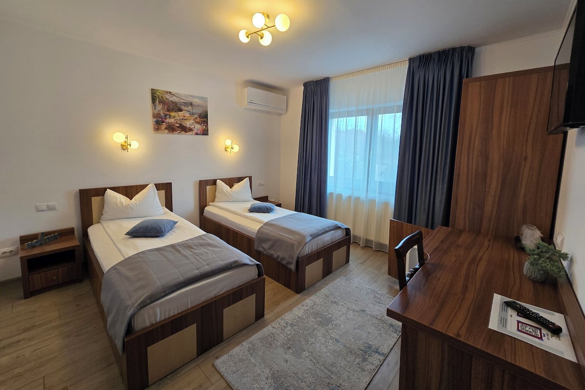 A hotel room with two beds, a desk, a chair, a TV, and a window with curtains.