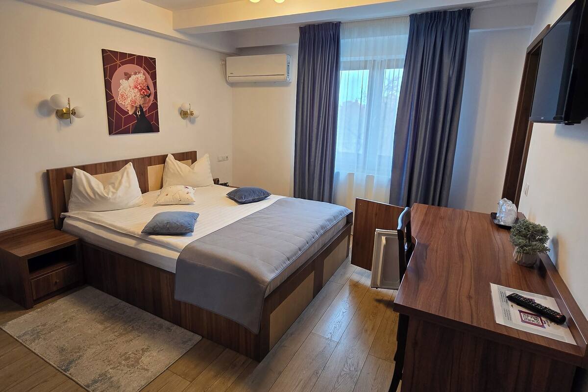 A hotel room with a bed, bedside table, desk, chair, and a TV.