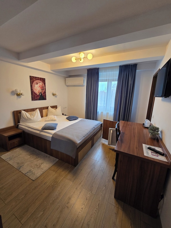 A hotel room with a bed, bedside table, desk, chair, and a TV. - Pensiunea Transilvania (Sibiu)
