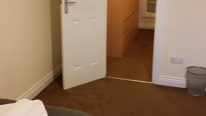 Hotellihuone, jossa on sänky, ovi, joka johtaa käytävään, ja roskakori.