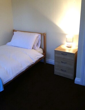 A single bed with white bedding, a wooden headboard, and a bedside table with a lamp. - Livingston Ideal Commuter Townhouse (Livingston)