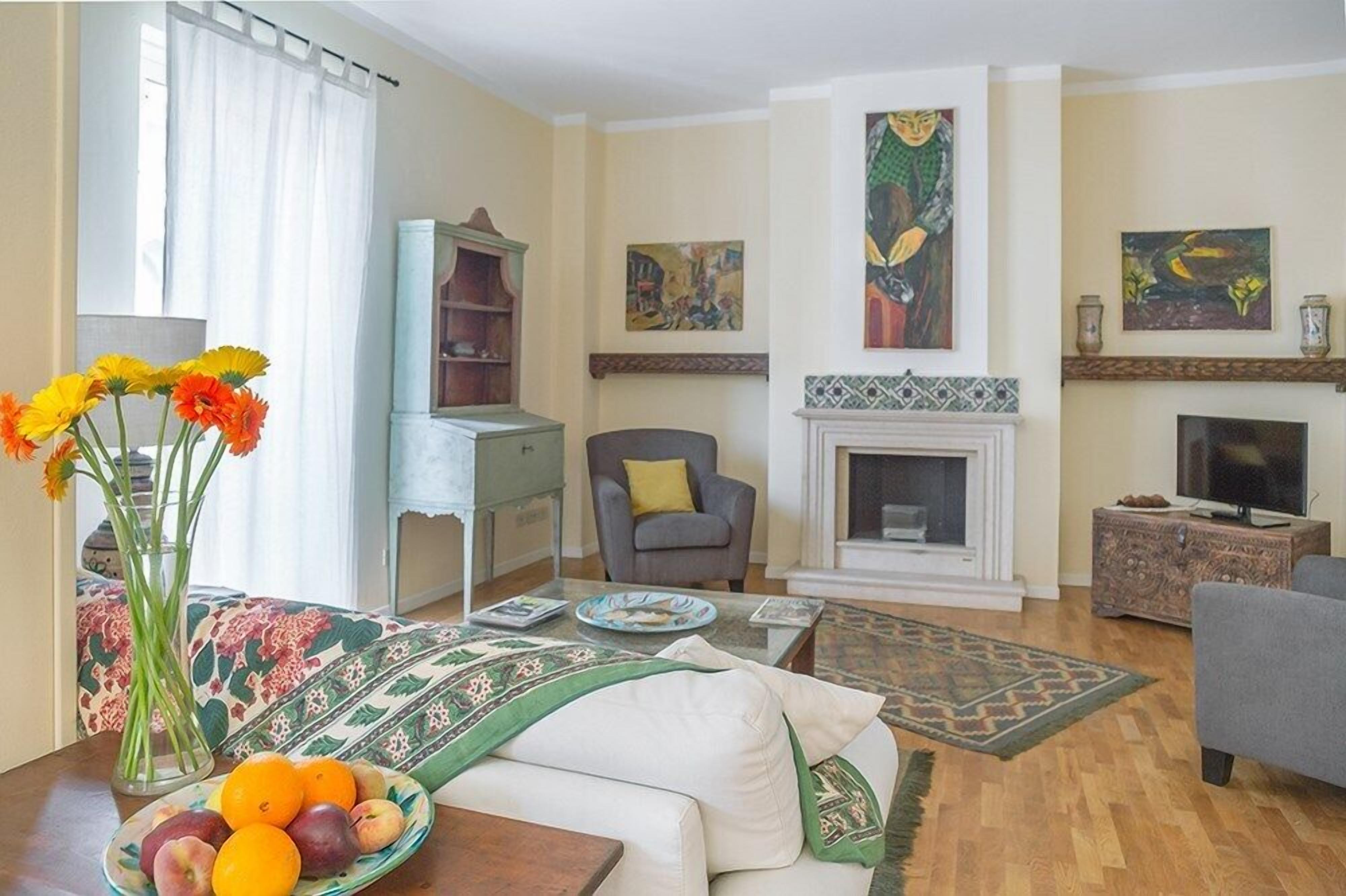 A living room with a fireplace, a television, a sofa, a coffee table with fruit, and a bookshelf.