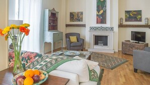 Uma sala de estar com lareira, televisão, sofá, mesa de centro com frutas e estante de livros.