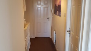 A hallway with a white door at the end, a radiator on the wall, and a painting above the door. - Livingston 4 Bedroom Townhouse (Livingston)