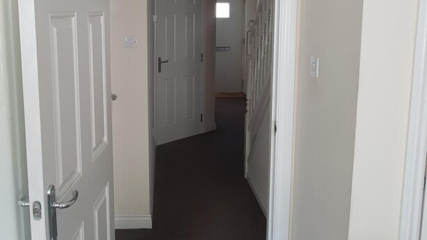 A narrow hallway with white doors, a dark carpet, and a ceiling light fixture. - Livingston 4 Bedroom Townhouse (Livingston)