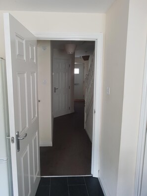 A narrow hallway with white doors, a dark carpet, and a ceiling light fixture. - Livingston 4 Bedroom Townhouse (Livingston)