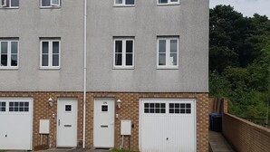 A two-story residential building with a flat roof, multiple windows, and two garage doors. - Livingston 4 Bedroom Townhouse (Livingston)