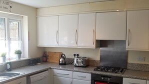 A modern kitchen with white cabinets, a gas stove, a dishwasher, and a red towel hanging on the oven. - Livingston 4 Bedroom Townhouse (Livingston)