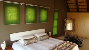 A bedroom with a large bed, a nightstand, a mirror, and green window treatments. - BushGlam Luxury Holiday Home (Hoedspruit)