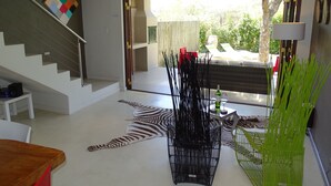 A modern living room with a staircase, a zebra-patterned rug, and a glass table with wine glasses and a bottle. - BushGlam Luxury Holiday Home (Hoedspruit)