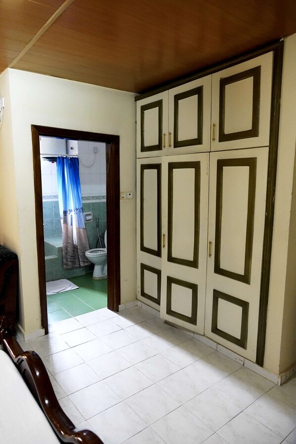 A bedroom with a bed, a wardrobe, and a bathroom visible through an open door. - Wusum Hotel (Makeni)