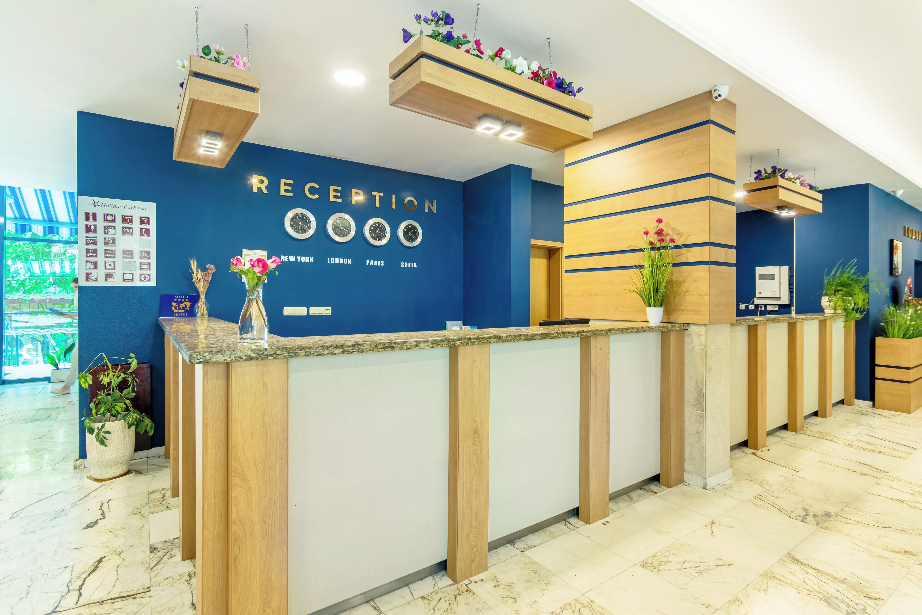 A reception area with a blue wall, wooden reception desk, and hanging flower baskets.