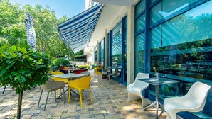 Une terrasse extérieure avec des chaises jaunes et blanches, une table et un parasol à rayures.