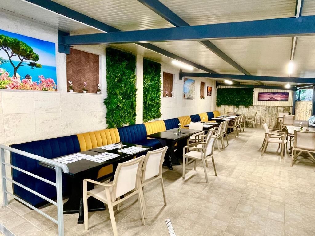 Un restaurante con mesas largas comunitarias y cabinas, jardines verticales verdes y un mural de un árbol y flores.