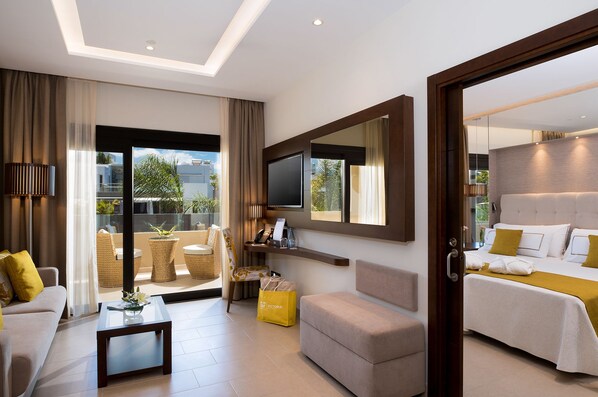 A modern hotel room with a sofa, a small table, a TV, and a bed with a yellow pillow. - GF Victoria (Adeje)
