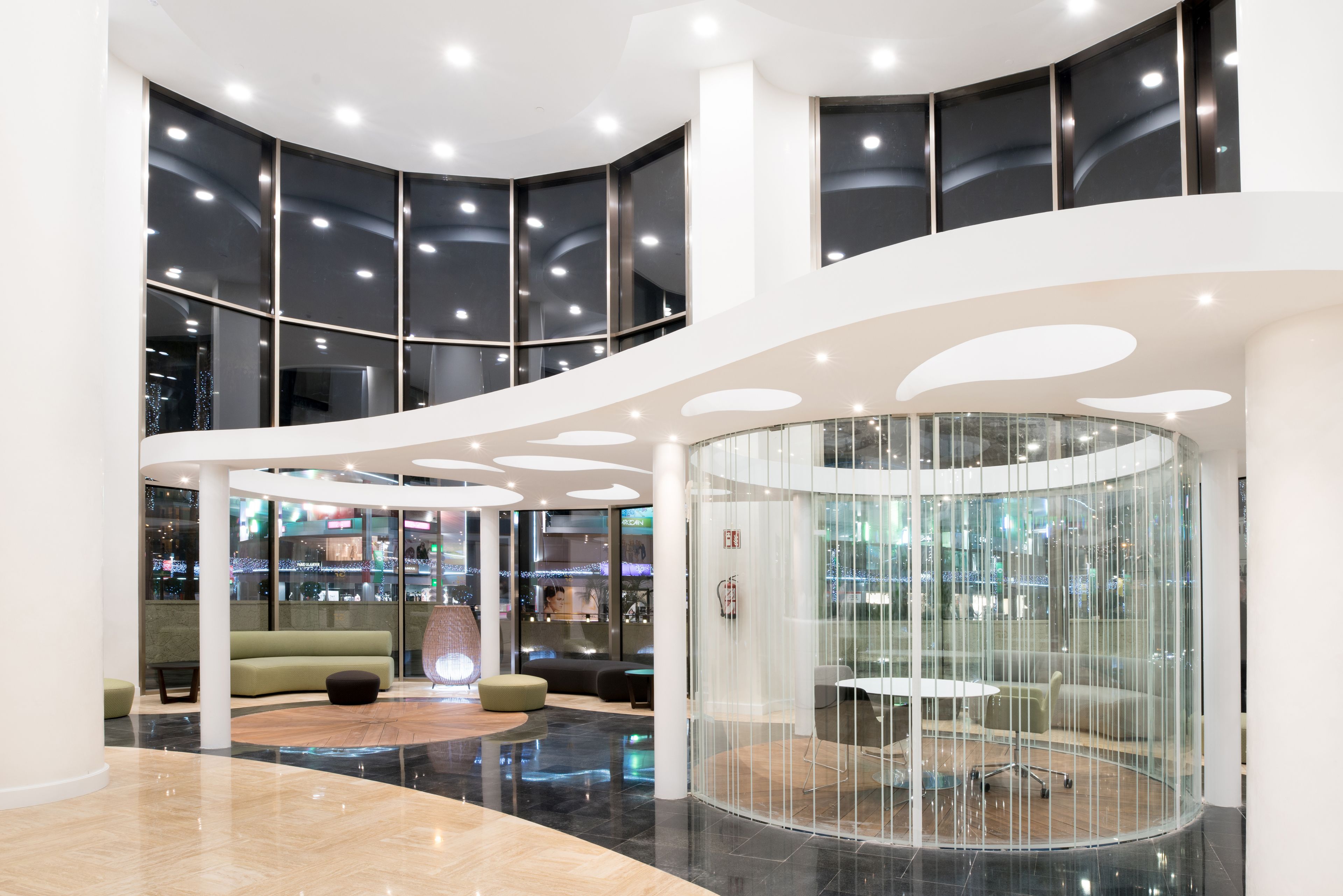 Un hall d’entrée moderne doté d’une verrière incurvée, d’espaces aménagés pour s’asseoir et offrant une vue sur le paysage urbain.