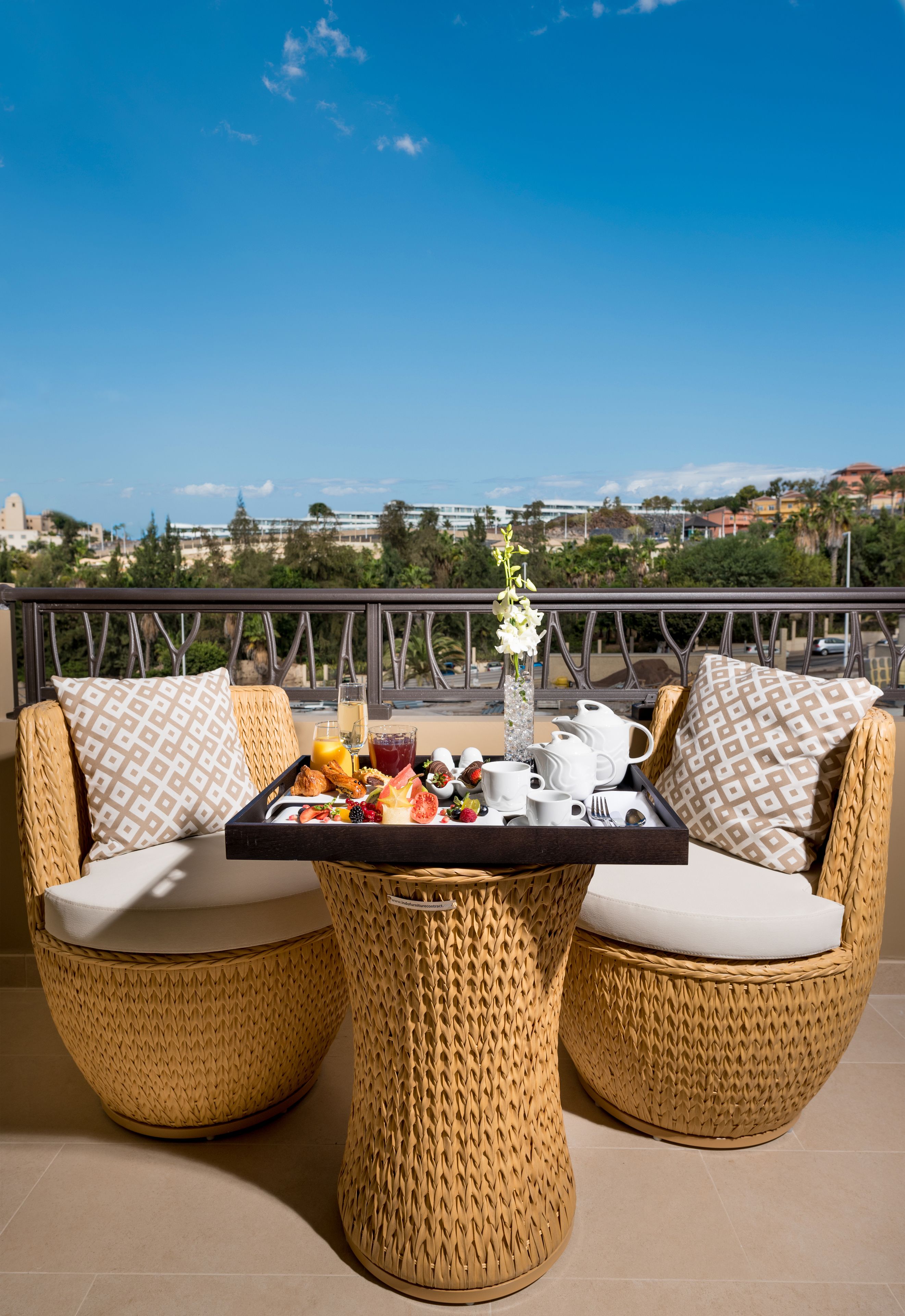 Een balkon met rieten meubels, een dienblad met ontbijtartikelen en een helder uitzicht op de stadszicht.