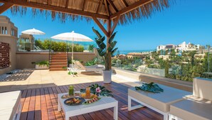 A wooden deck with a thatched roof, white furniture, and a table set with food and drinks. - GF Victoria (Adeje)