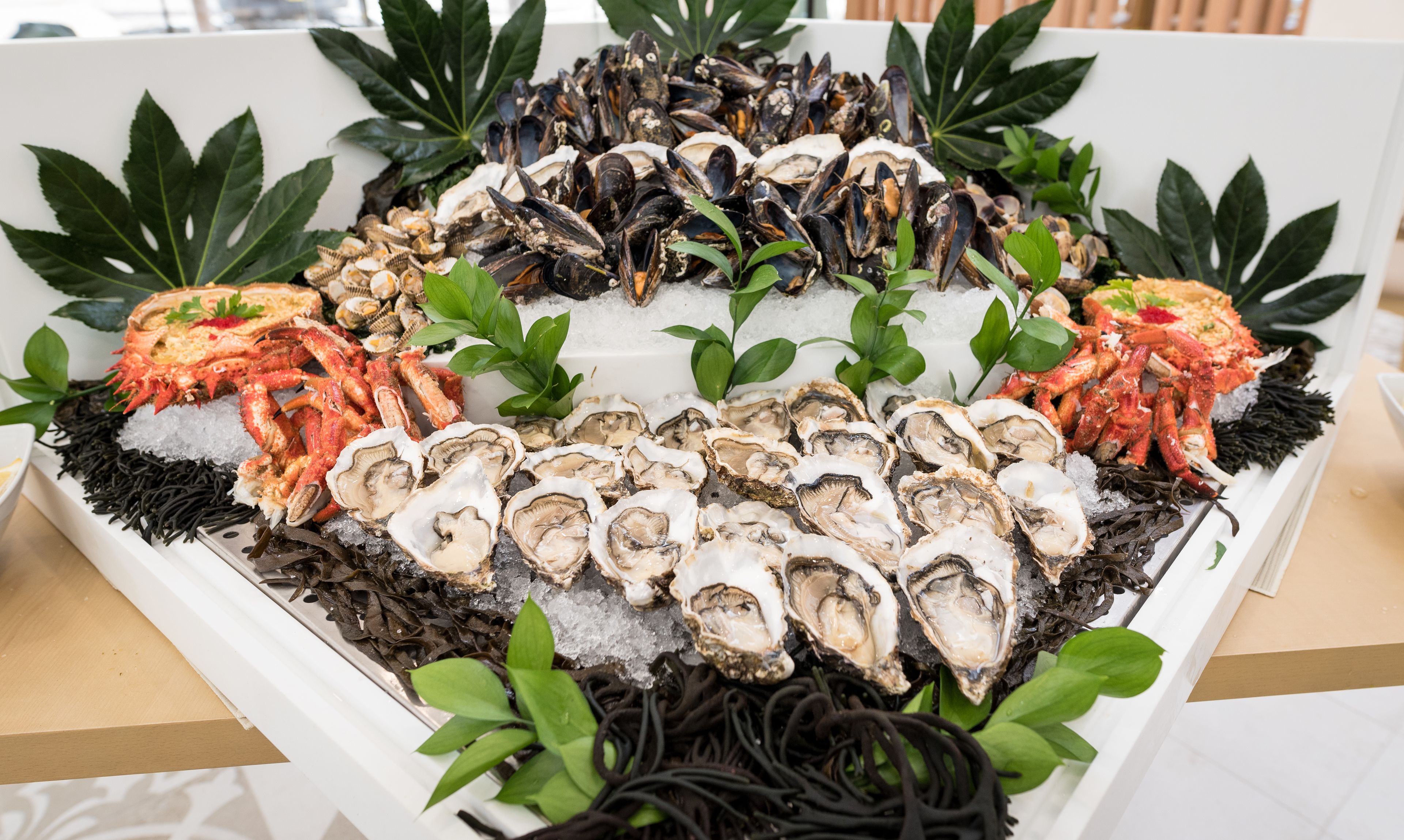 Een visplateau met oesters, mosselen en krabbenpoten, omgeven door groene bladeren en ijs.