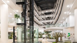 A multi-level atrium with glass railings, a central elevator, and a decorative tree sculpture. - GF Victoria (Adeje)