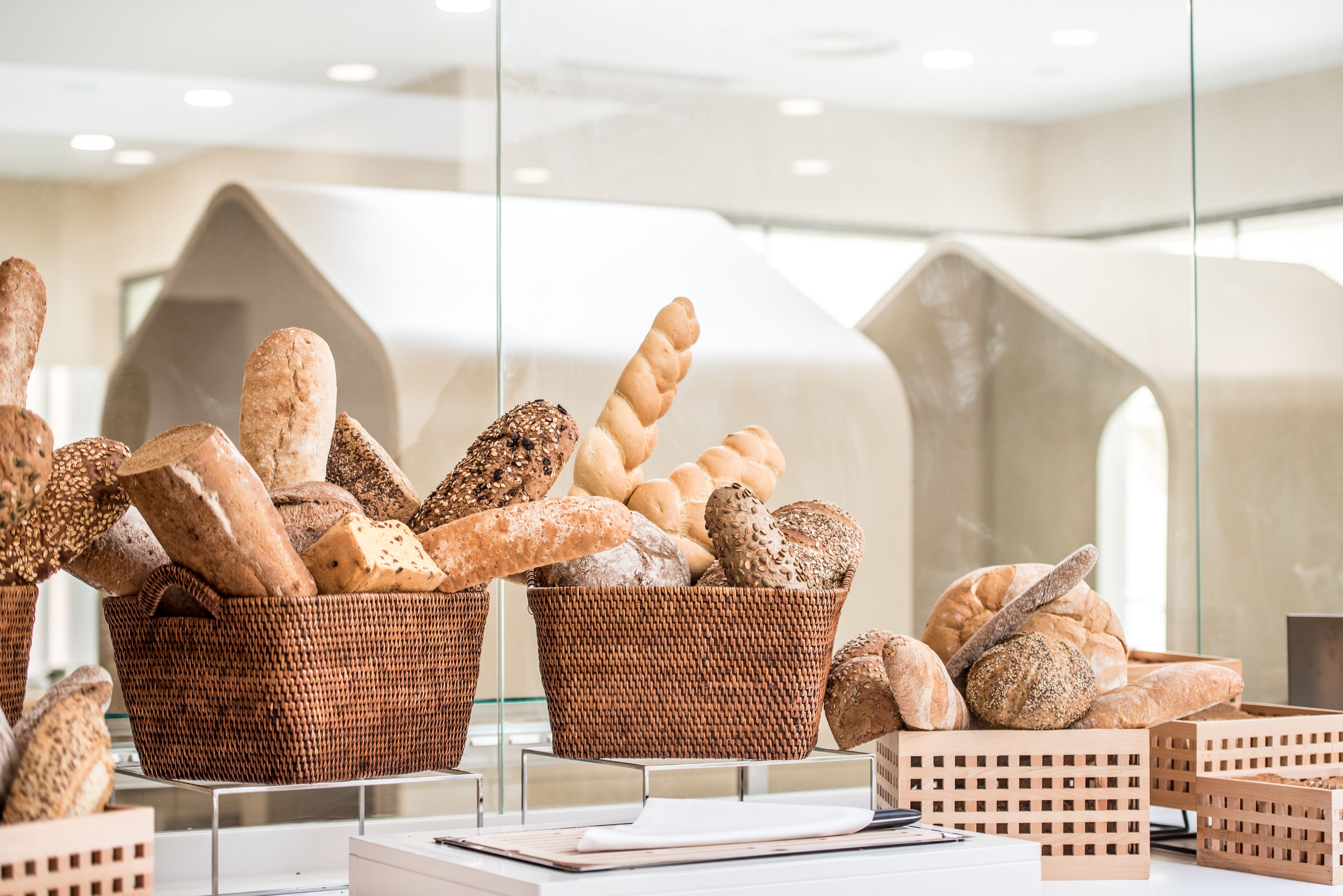Wicker baskets filled with various types of bread displayed in a modern setting with geometric architectural elements.