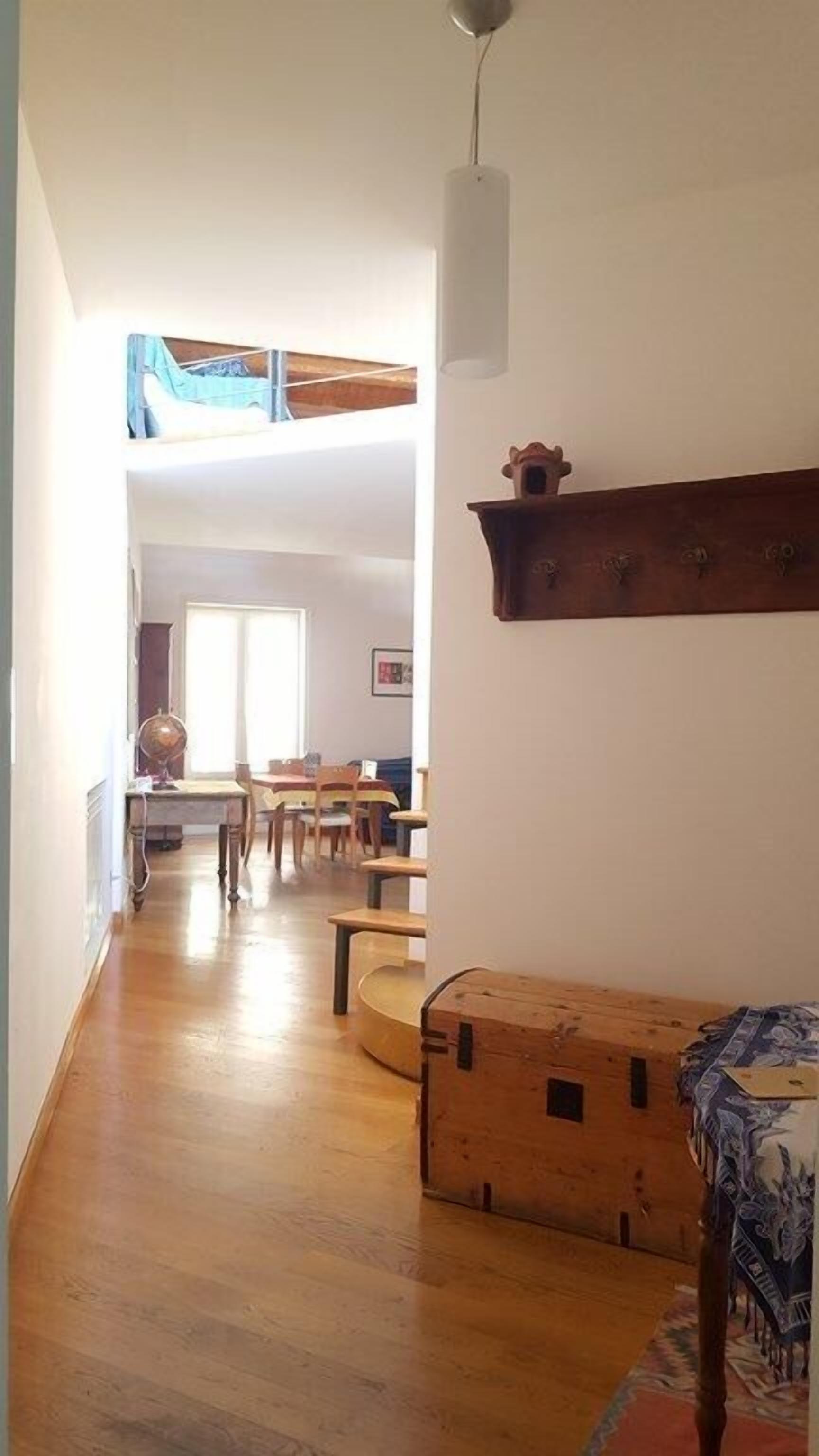 Een ruime kamer met houten vloer, een eethoek met stoelen en een tafel, en een bed met een bedekt patroon.