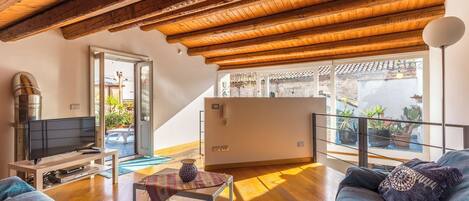A spacious living area with a wooden ceiling, a television, a sofa, and a coffee table.