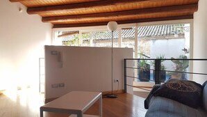 A room with a wooden ceiling, a balcony with potted plants, a sofa, and a table.