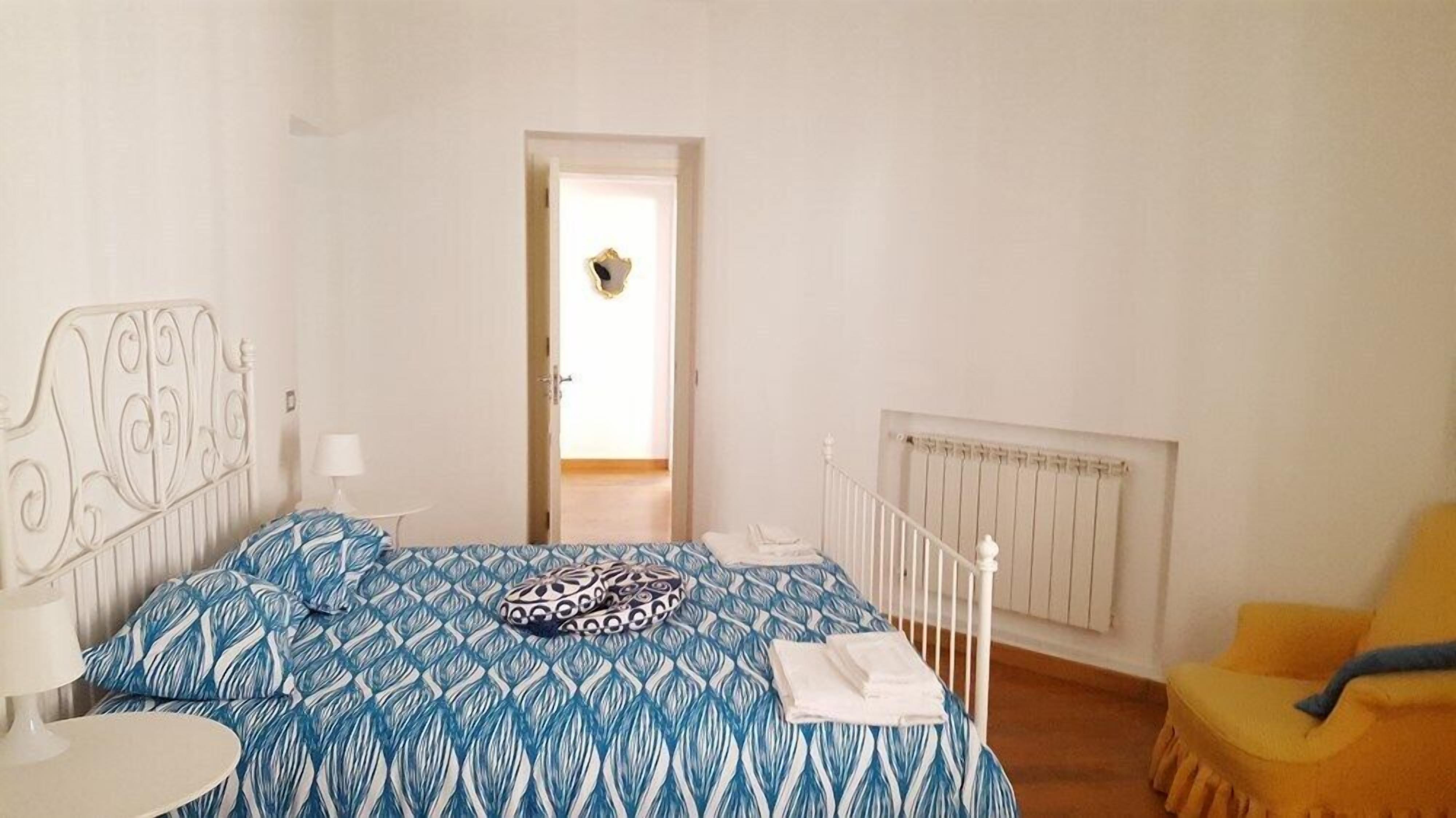 A bedroom with a bed, a chair, a radiator, and a door leading to another room.