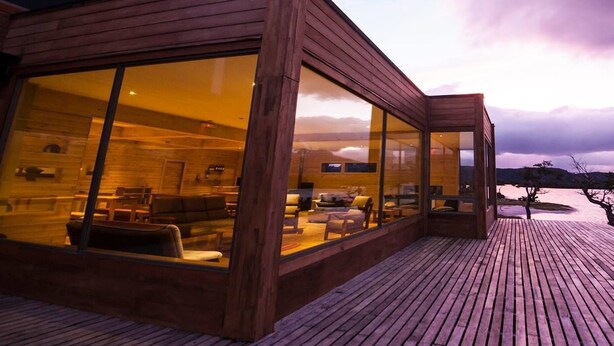 Una cabaña moderna de madera con amplios ventanales, una terraza de madera y vistas del paisaje.