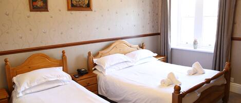 A hotel room with two single beds, a wooden headboard, a nightstand with a phone, and a window with curtains.