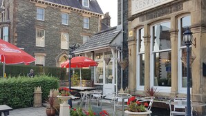An outdoor seating area with tables and chairs, a flower bed, and a building labeled "The Keswick Park Hotel." - Keswick Park Hotel (Keswick)