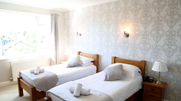 A bedroom with two single beds, a nightstand with a lamp, and a window with curtains.