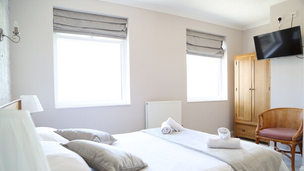 A hotel room with a bed, a chair, a wardrobe, and a television. - Keswick Park Hotel (Keswick)