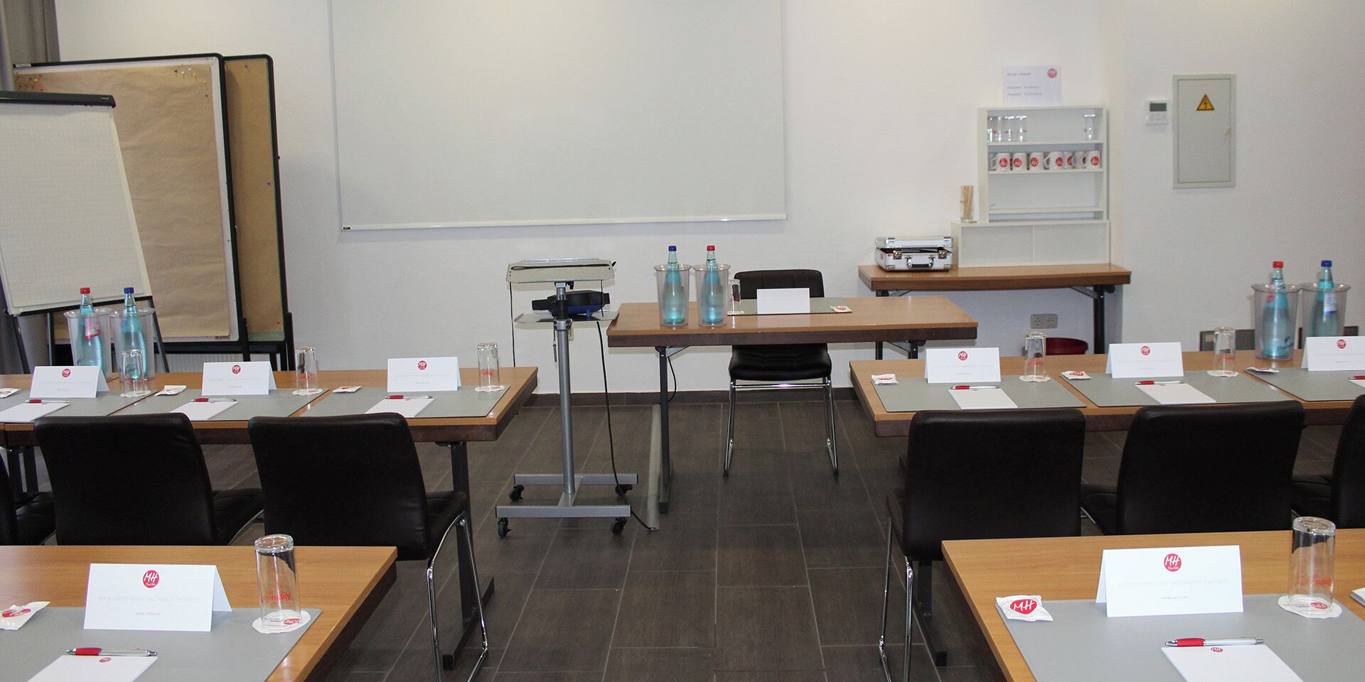 A conference room with multiple tables, chairs, nameplates, water bottles, and a projector screen.