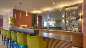 A modern bar area with a long counter, yellow bar stools, and a mirrored wall displaying bottles. - ACHAT Hotel Frankfurt Maintal (Maintal)