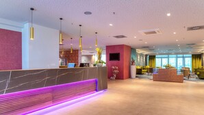 A modern hotel lobby with a marble reception desk, a seating area with a neon-lit bench, and a dining space with yellow chairs. - ACHAT Hotel Frankfurt Maintal (Maintal)