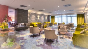 A modern hotel lobby with a marble reception desk, multiple seating areas with yellow and grey upholstered chairs, and large windows with curtains. - ACHAT Hotel Frankfurt Maintal (Maintal)