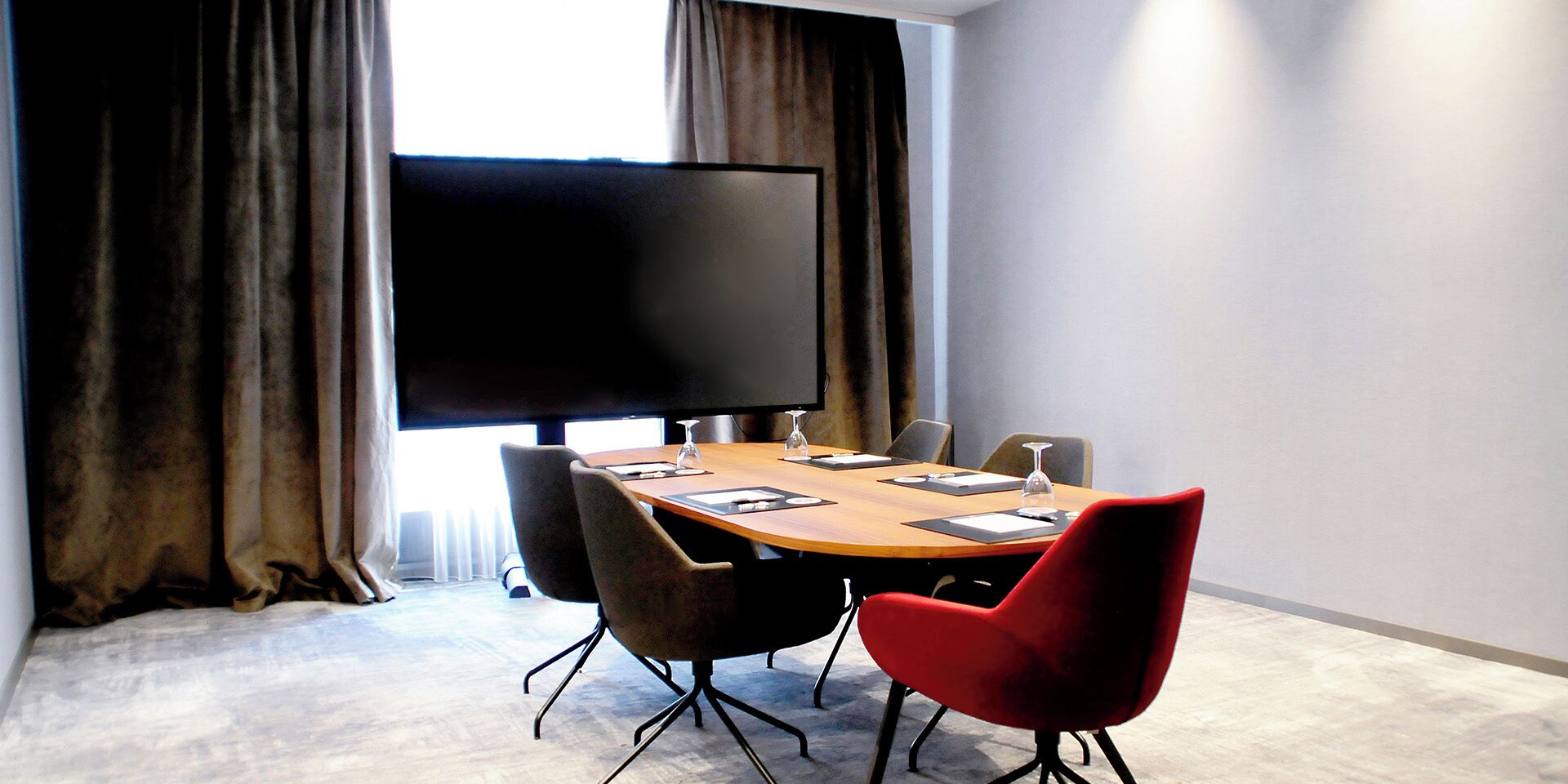 Een vergaderruimte met een grote tafel, stoelen, een flatscreen-tv en gordijnen.