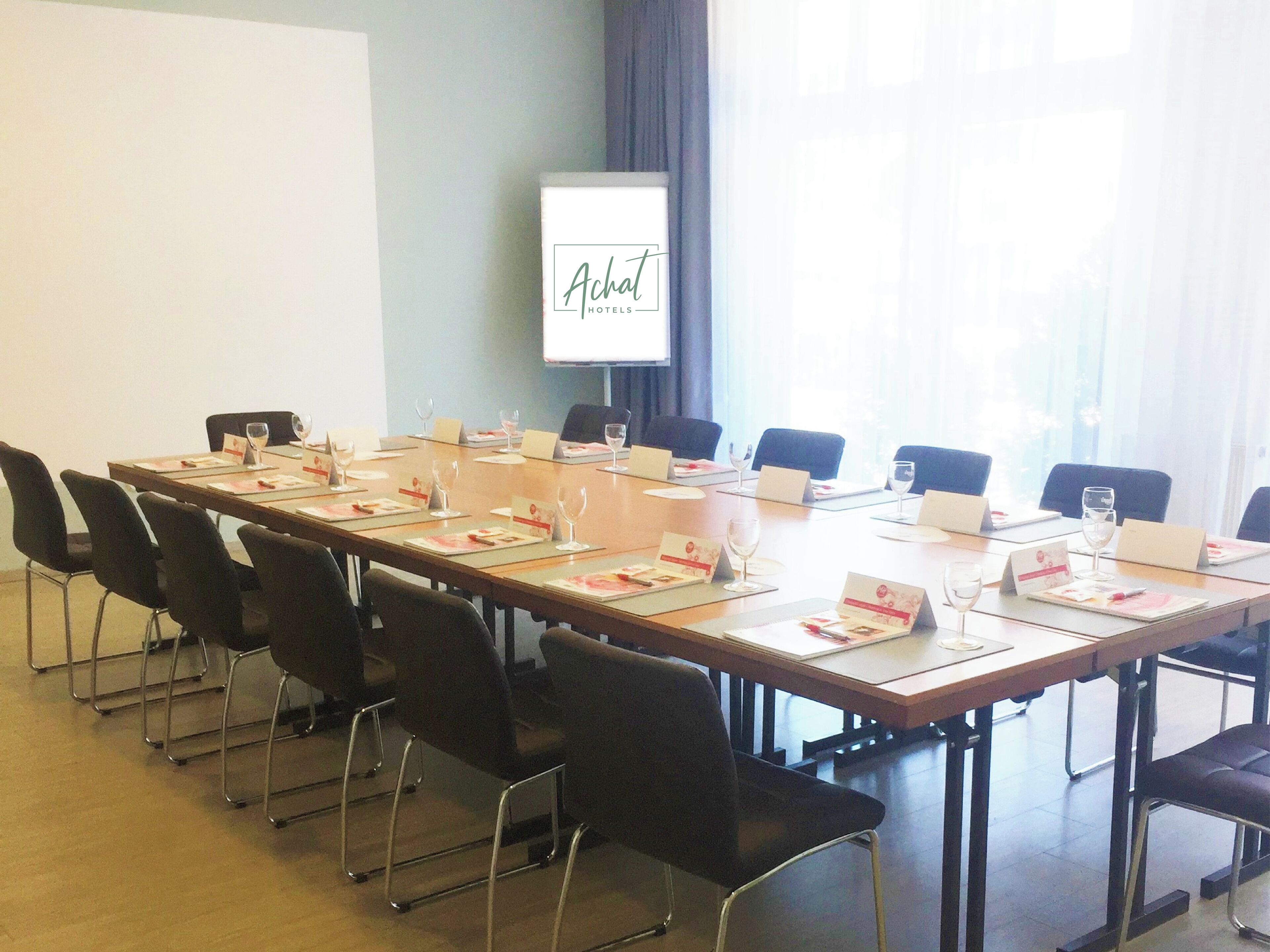 Une salle de conférence avec une longue table, des chaises, des porte-noms et des verres à vin.