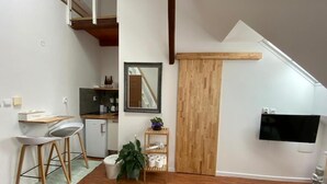 A modern kitchen with wooden flooring, a dining area with stools, a small refrigerator, and a wooden door. - Pension Skylark (Pardubice)