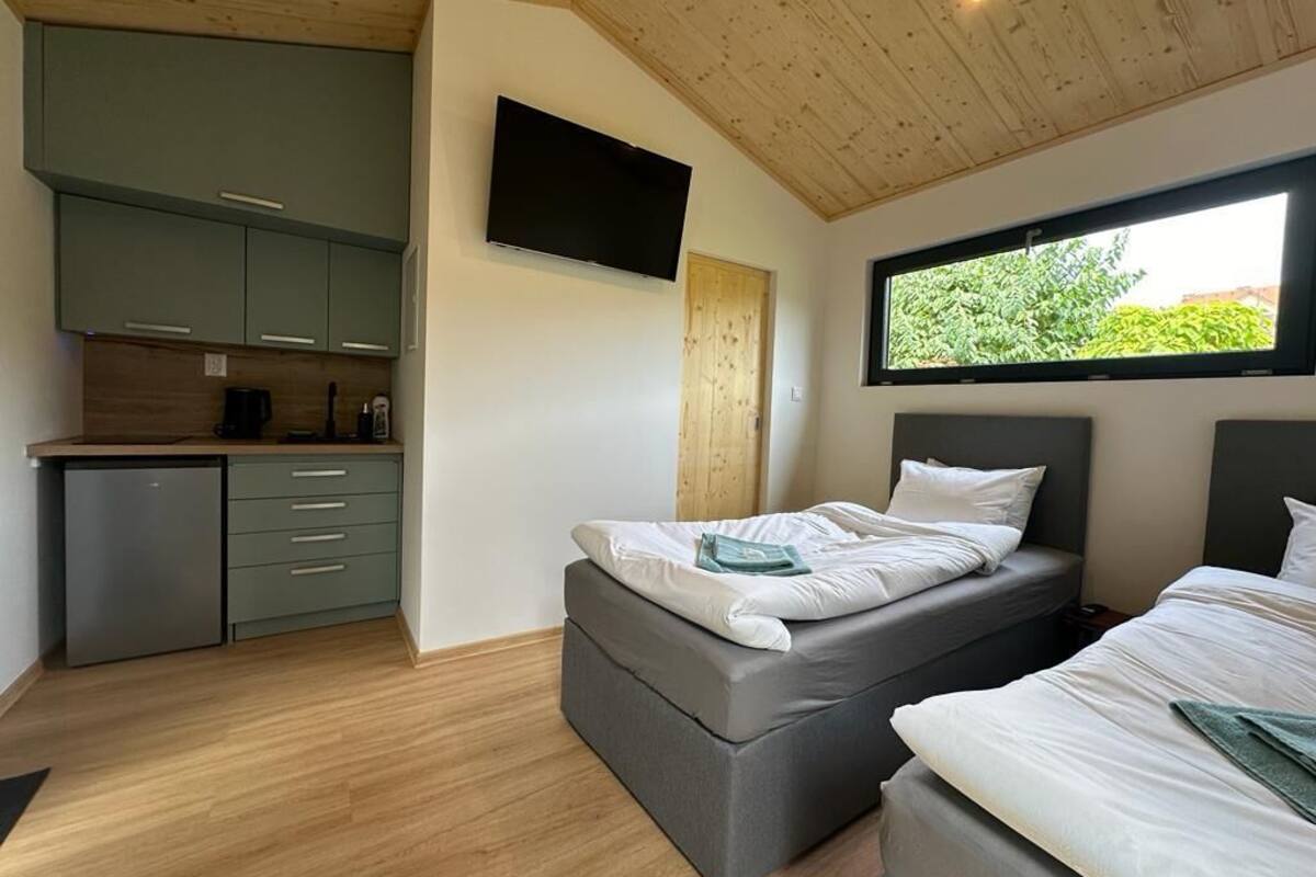 A compact room with a bed, a small kitchenette, and a TV mounted on the wall.