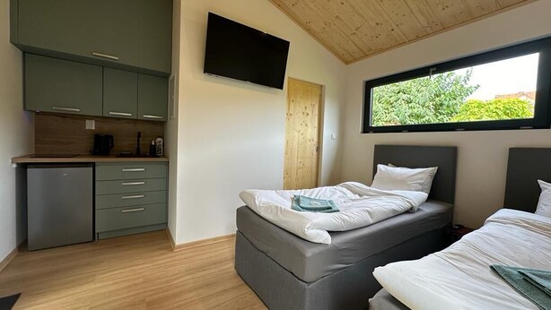 A compact room with a bed, a small kitchenette, and a TV mounted on the wall. - Pension Skylark (Pardubice)