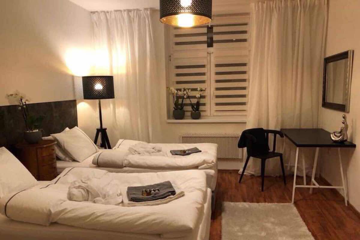 A hotel room with two beds, a desk, a chair, a lamp, and a window with curtains.