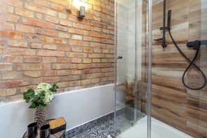 A modern bathroom with a brick wall, a glass shower enclosure, and a small table with a vase and cups. - Pension Skylark (Pardubice)