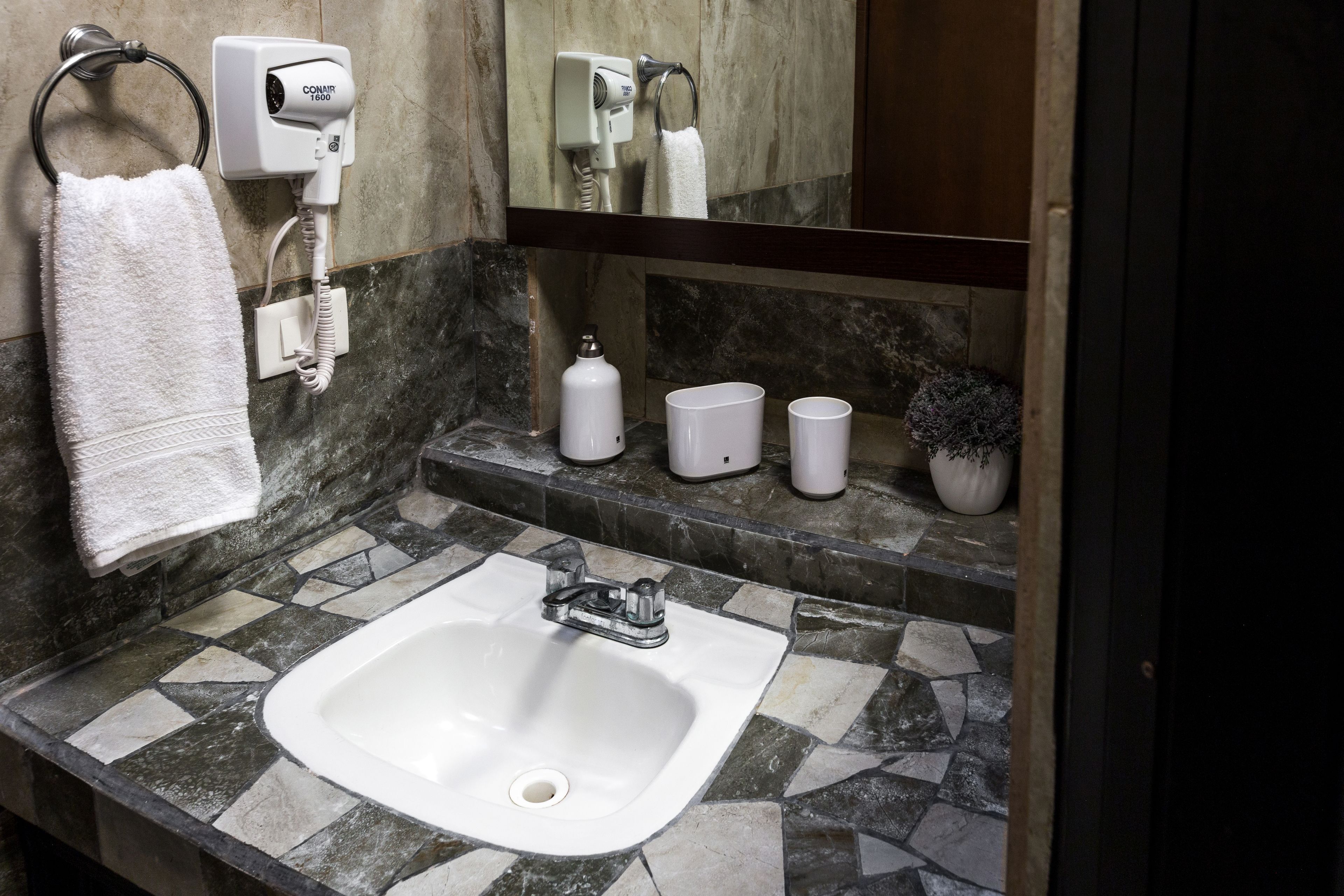 Une salle de bain avec un lavabo blanc, un porte-serviettes, un sèche-cheveux et un miroir.